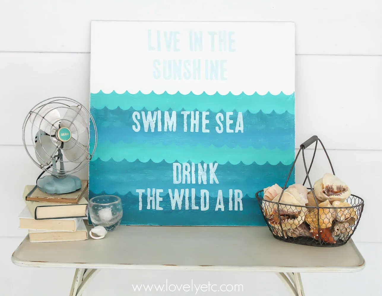wooden sign with handpainted waves next to basket of shells.