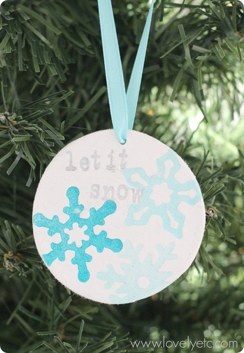 DIY stamped clay ornament stamped with snowflakes and the words let it snow hanging on tree.