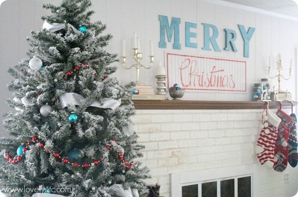 Christmas tree with aqua red and white christmas decorations next to white painted fireplace with Merry Christmas sign.