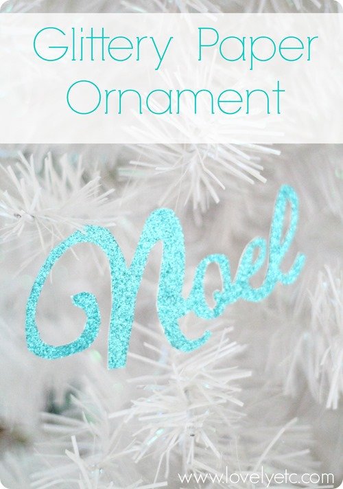 glittery paper ornament that says Noel hanging on white Christmas tree.