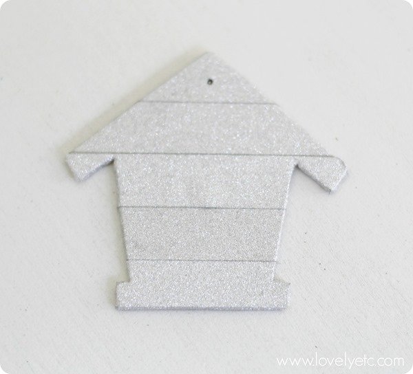 birdhouse shape covered in silver washi tape to create the background of a DIY nativity ornament.
