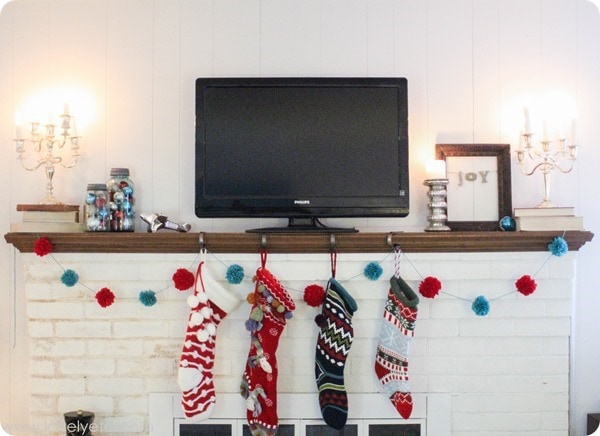 aqua and red christmas mantel with colorful stockings, pom pom garland, and jars of ornaments.