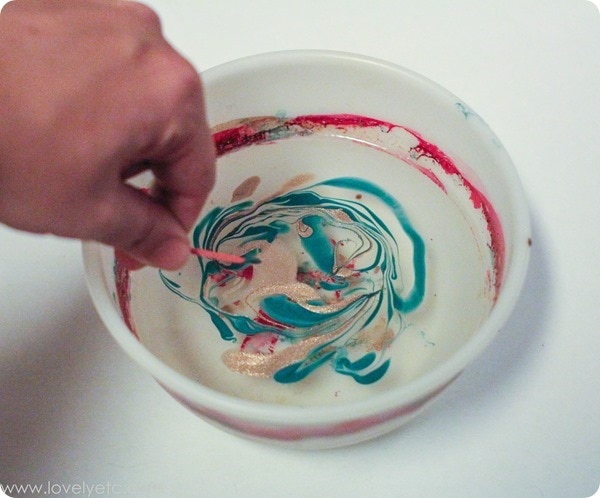 using a toothpick to swirl nail polish in water to marble Christmas ornaments.