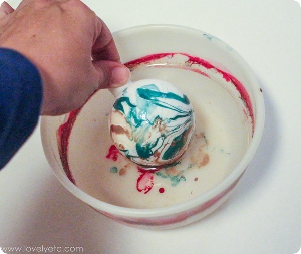 pulling a marbled ornament out of a bowl of water.