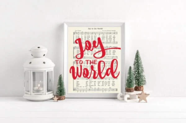 Joy to the world music printable with red script that says Joy to the World, framed next to mini Christmas trees.