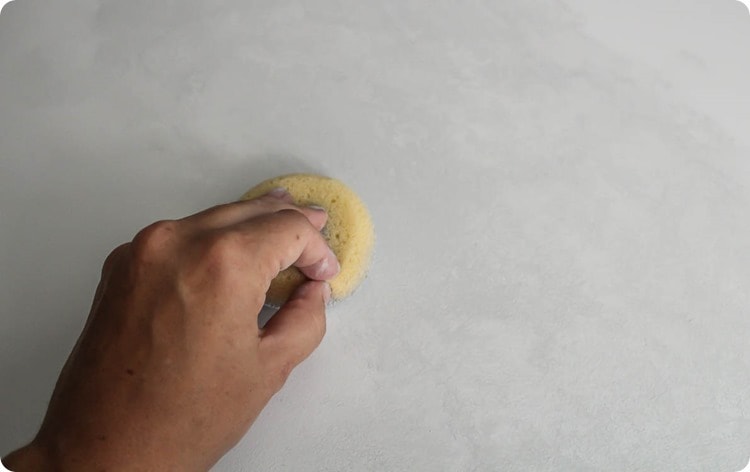 hand holding a sponge, dabbing gray paint onto painted countertop