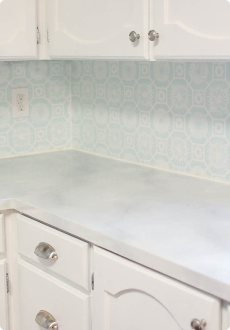 kitchen with laminate countertop painted like marble, painted white cabinets, and a painted backsplash