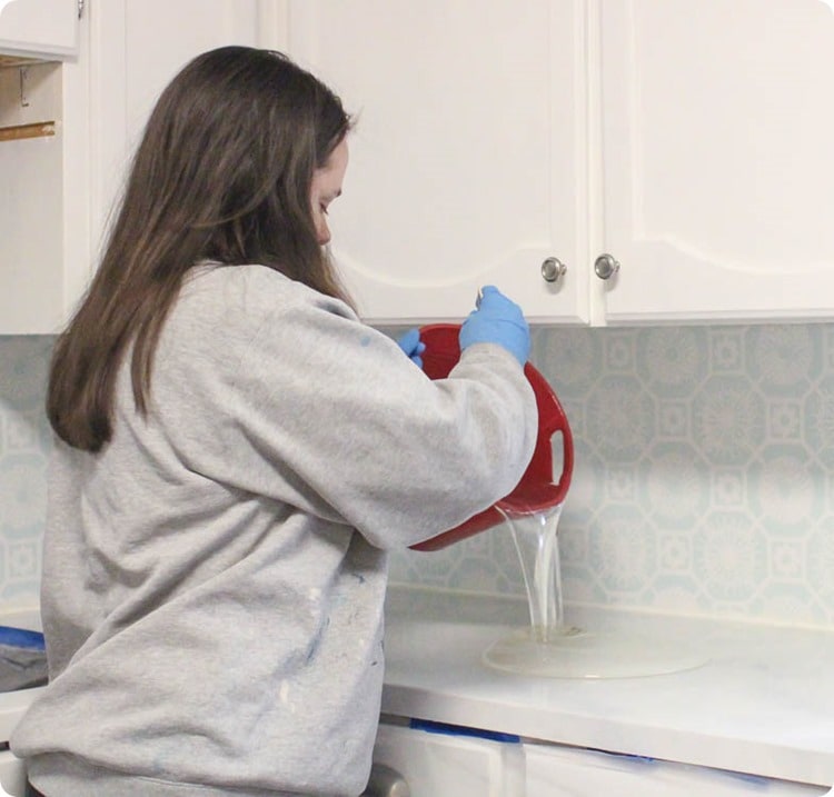 Woman pouring envirotex lite from a bucket onto painted countertops