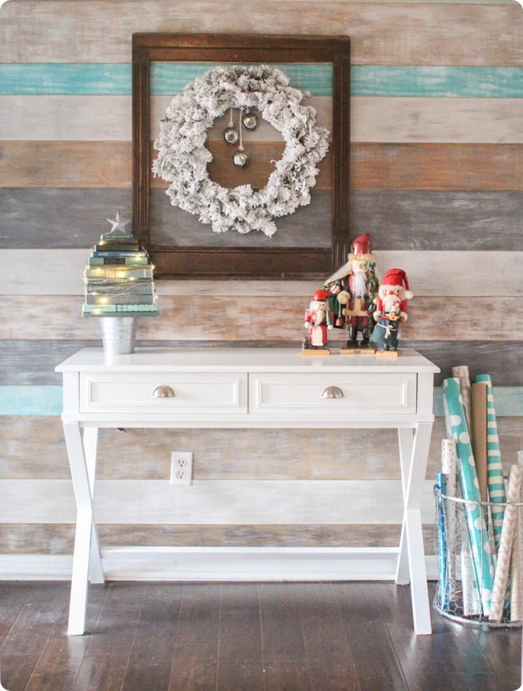 Entryway with wood plank wall, flocked wreath in frame, nutcrackers, and Christmas tree made from old books.