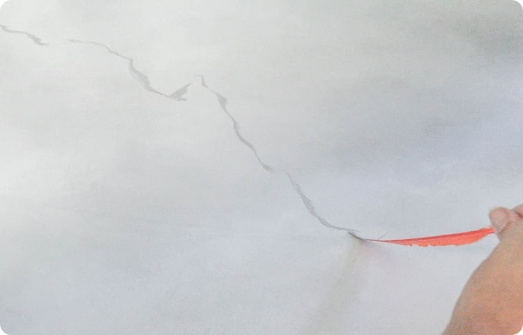 a hand holding a feather, drawing gray marble lines on countertop with paint