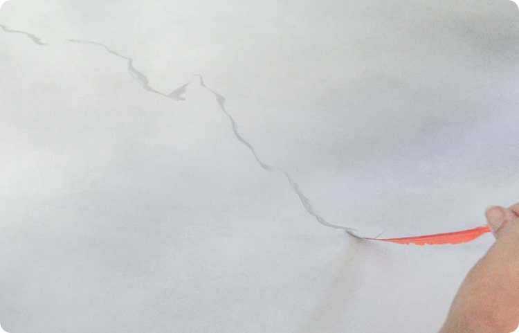a hand holding a feather, drawing gray marble lines on countertop with paint