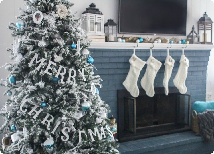 flocked Christmas tree with Merry Christmas banner next to blue fireplace.