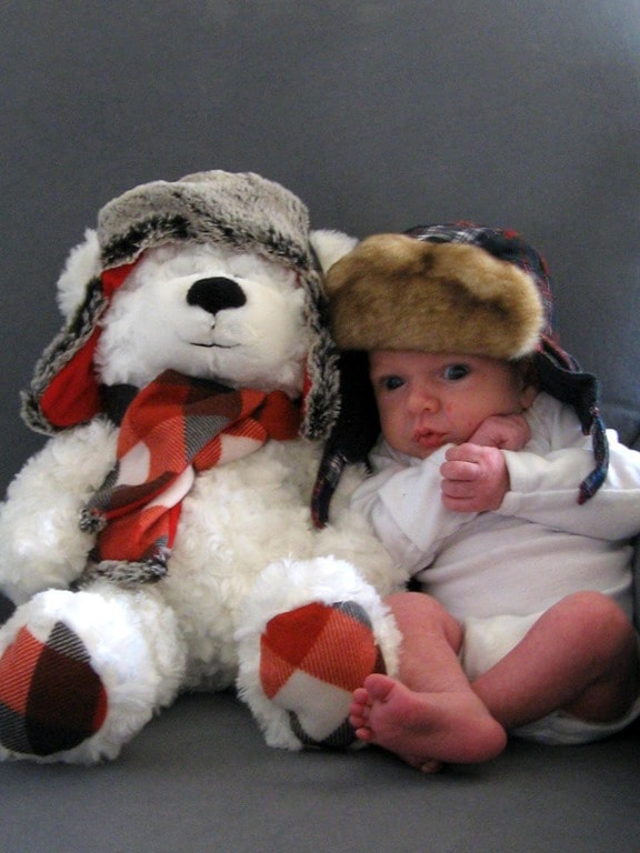 small baby wearing a Christmas hat next to a stuffed bear.