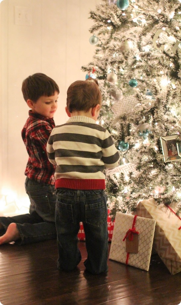 two kids standing in front of Christmas tree looking at ornaments.