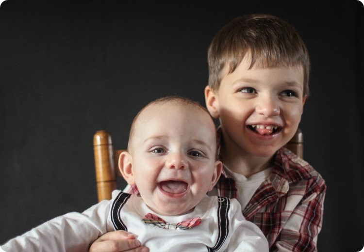 Christmas photo of brothers smiling in a little chair.