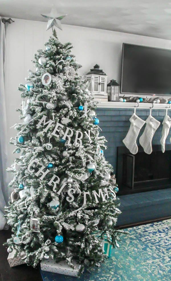 Flocked Christmas tree with blue and silver ornaments and a glittery Merry Christmas banner.