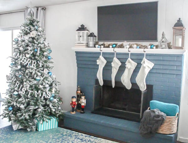Flocked Christmas tree with Merry Christmas banner next to blue fireplace with white stockings.