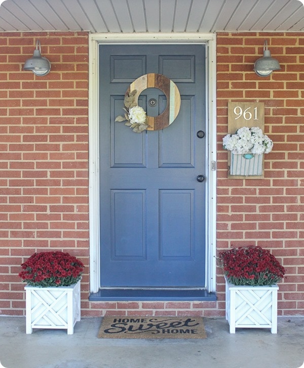 ugly brick ranch with a blue front door  and 2 planters with mums