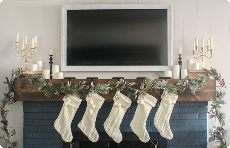 christmas mantel with white stockings, white candles, and tv