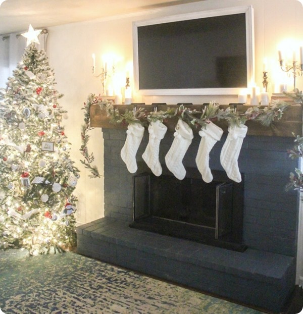 Christmas mantel with glowing candles next to lit Christmas tree.