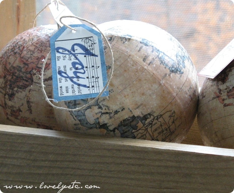 DIY joy to the world ornament made using a globe ornament and a sheet music tag that says Joy.