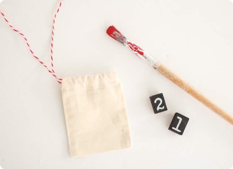 materials to make reusable advent calendar - muslin treat bags, number stamps, and paintbrush with red paint.