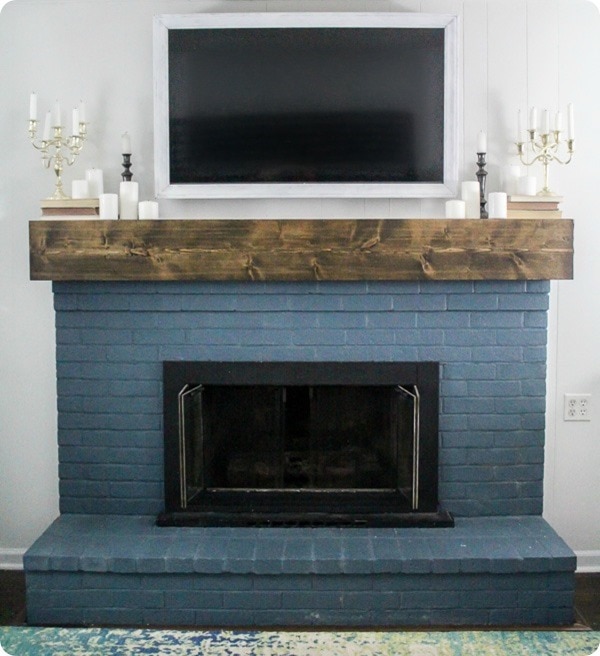 How to make a cheap and easy DIY white TV frame. This TV frame is simple, lightweight, and swivels with your TV. DIY white TV frame shown hanging over blue brick painted fireplace.