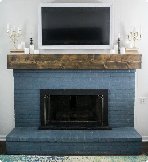 DIY white TV frame shown hanging over blue brick painted fireplace.