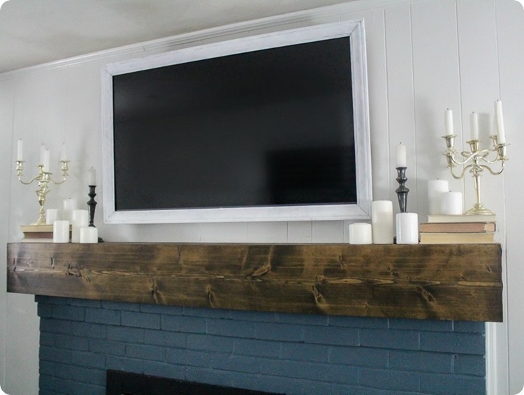 white pained tv frame hanging over brick fireplace.