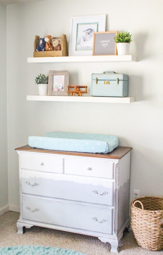 Gray and white dresser changing table with floating shelves in nursery.