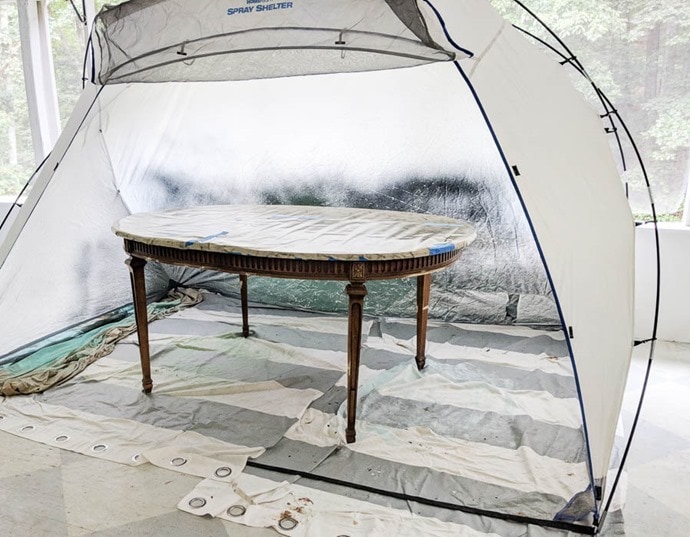 painting a table with a paint sprayer in a paint shelter
