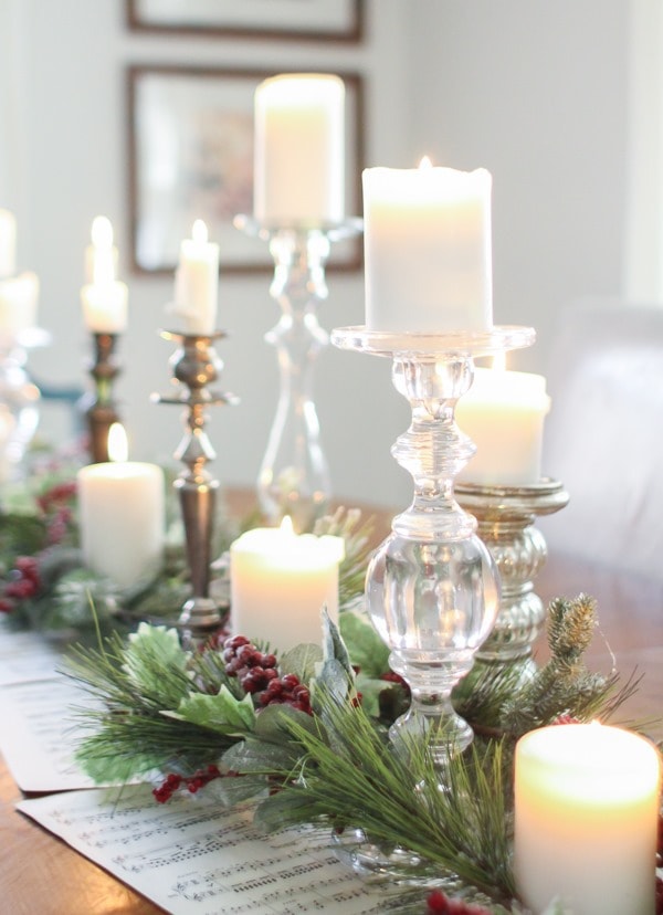 close up of Christmas centerpiece made with flocked Christmas garland, glass and siren candlesticks, and pillar candles.