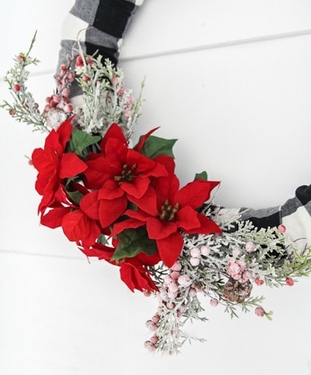 plaid Christmas wreath with flocked greenery and red poinsettias attached.