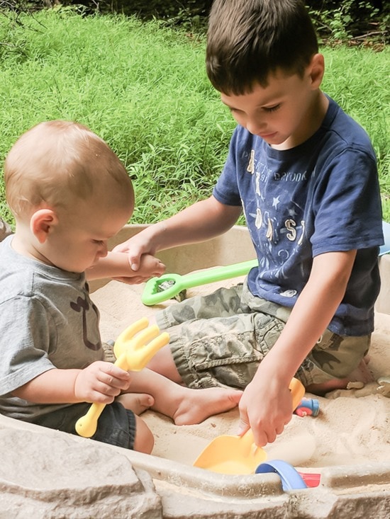 baby and big brother playing in sand box.