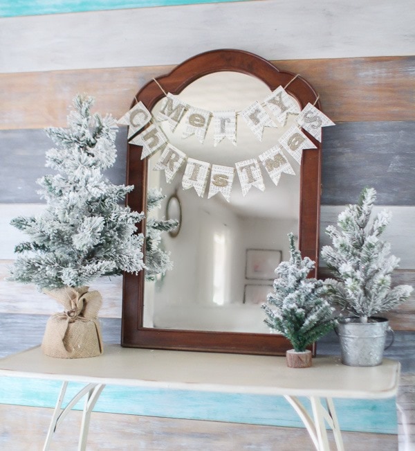 vintage mirror against wood plank wall decorated with mini flocked Christmas trees.