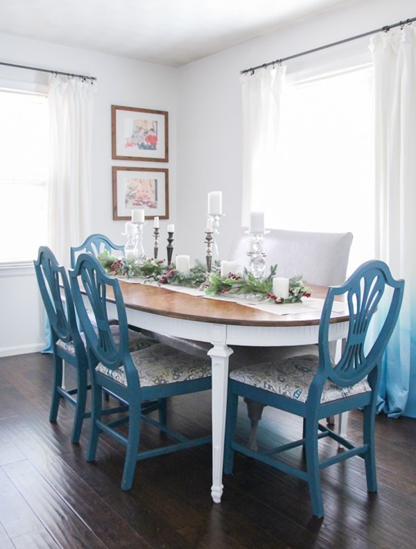 Dining room table with simple Christmas centerpiece of sheet music, Christmas garland, and candlesticks.