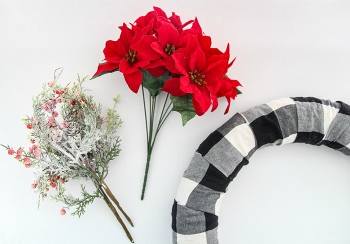 plain buffalo plaid covered wreath form next to Christmas picks and poinsettias.