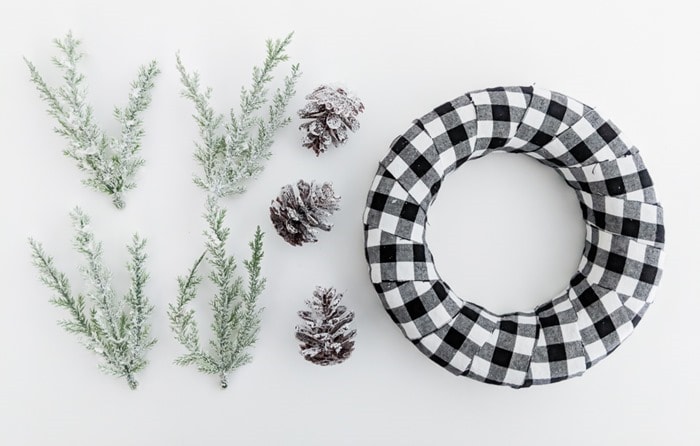 plaid wreath next to small pieces of faux greenery and pinecones.