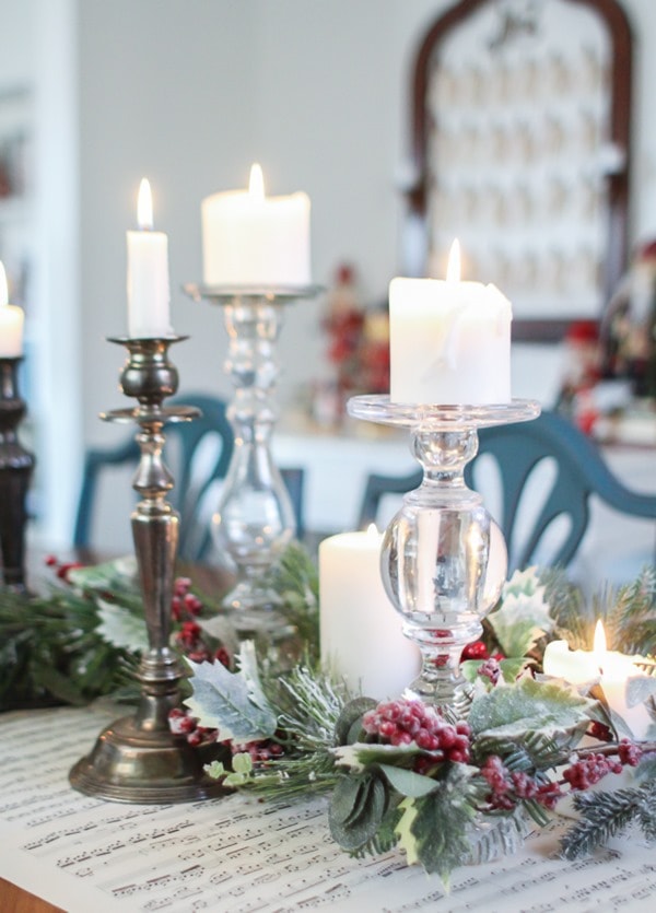 close up of Christmas centerpiece made with flocked Christmas garland, vintage candlesticks, and pillar candles.