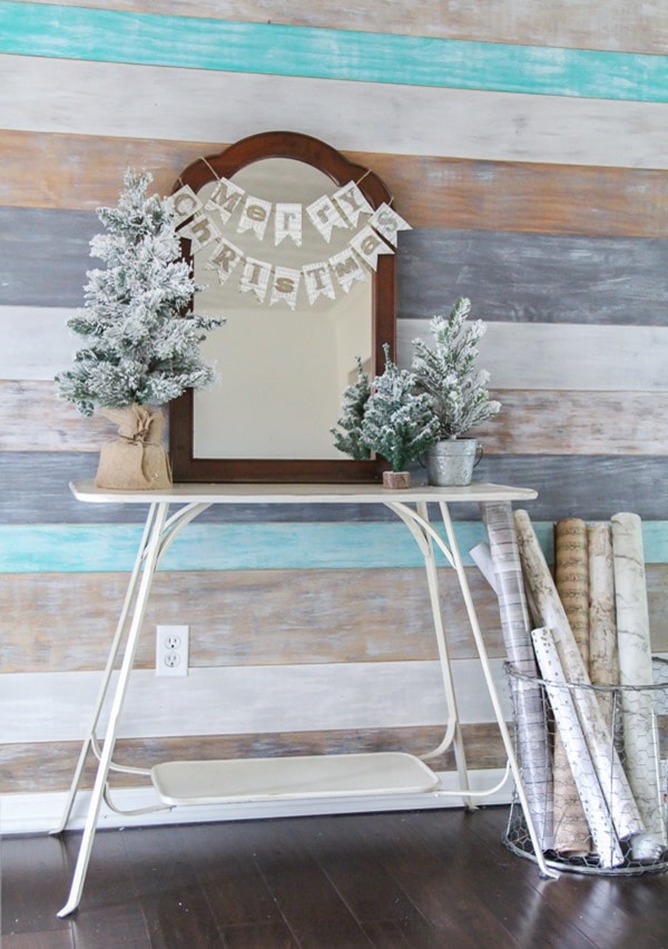 Simple farmhouse Christmas decor in the entry - glitter Merry Christmas banner on old mirror with mini flocked trees and a basket of wrapping paper.