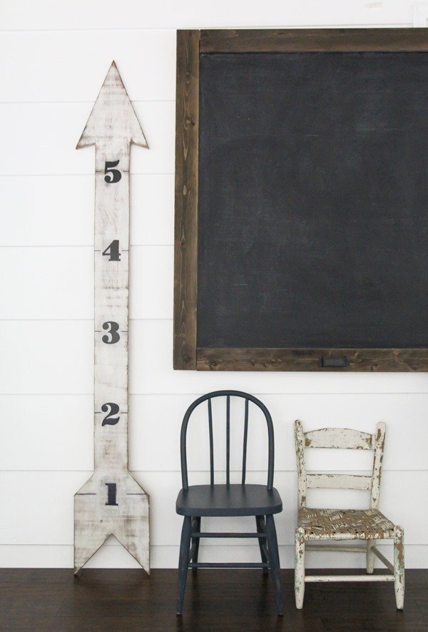 large DIY chalkboard next to wooden arrow growth chart and two children's chairs