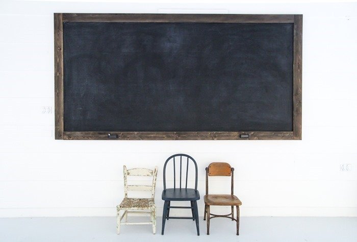 large diy chalkboard hanging on white wall above three childrens chairs