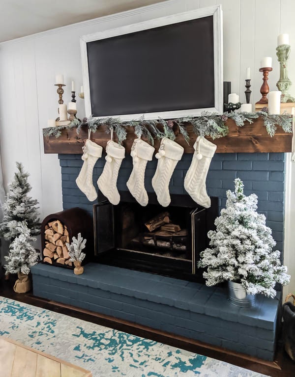This neutral Christmas fireplace is full of beautiful Christmas touches including mini flocked Christmas trees, a unique firewood holder, and cable knit stockings.