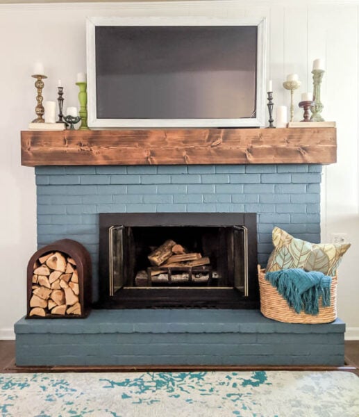 DIY fireplace facelift with painted blue brick, DIY chunky wood mantel, DIY TV frame, and upcycled firewood holder.