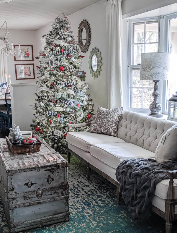 Flocked Christmas tree decorated with ribbon and white and red ornaments next to a cream couch in the living room.