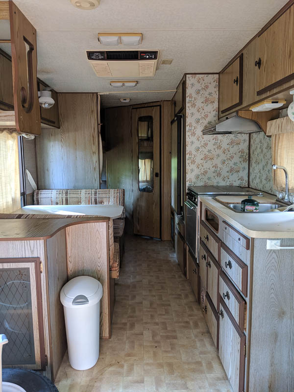 interior of 1986 jayco camper with fading woodwork, wallpaper, and plaid upholstery