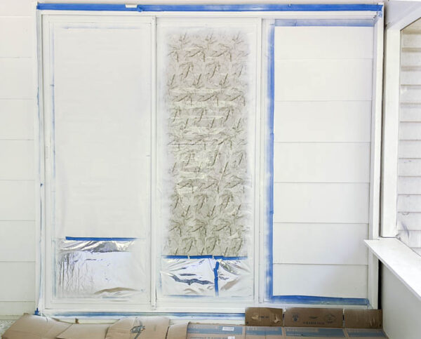 sliding glass doors with a layer of white paint, surrounded by painter's tape and paper