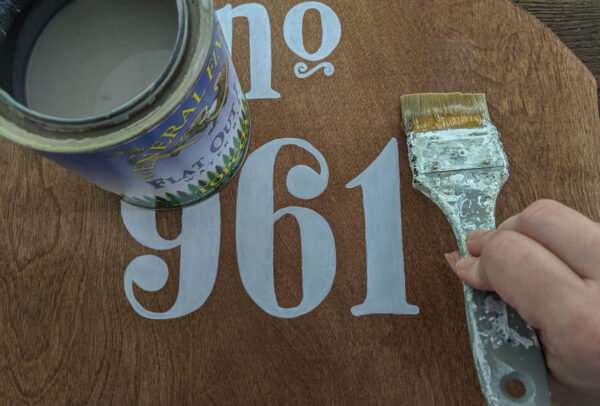 painting sealer onto plywood house number with a paintbrush