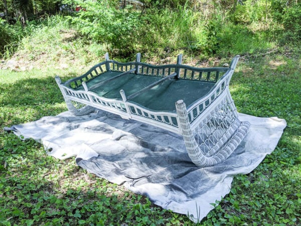 wicker sofa upside down on a drop cloth, ready for paint