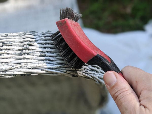removing peeling paint from a wicker chair using a stiff stripping brush